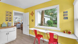 Una habitación luminosa de color amarillo con una ventana, un escritorio blanco y sillas rojas.