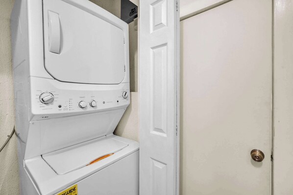 A white wall-mounted washer and dryer unit with control knobs and a yellow caution label.