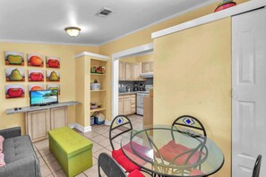 Un espacio habitable compacto con kitchenette, una zona de comedor con mesa de vidrio y sofá.