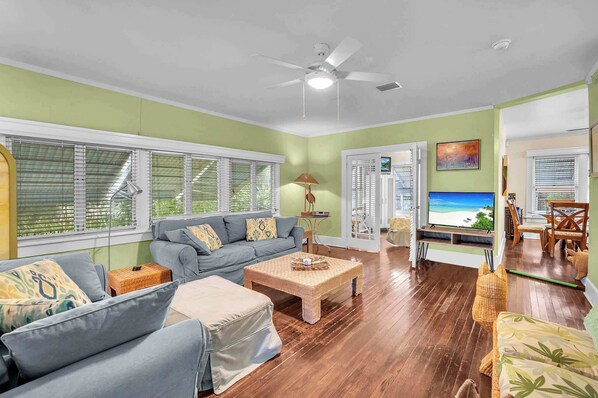 A spacious living room with a grey sofa, a coffee table, and a TV screen displaying a beach scene.