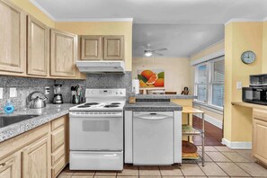 A kitchen with wooden cabinets, a white stove, granite countertops, and a ceiling fan.