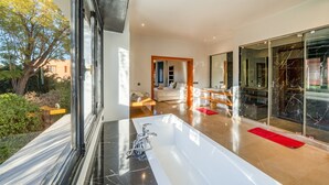 Et moderne badeværelse med et stort badekar, en glas brusekabine og udsigt til den udendørs have.