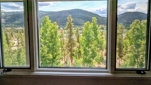 A room with a large window offering a view of a forested area and distant mountains.