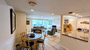 A modern kitchen with granite countertops, a dining area with a round table and chairs, and a living room with a sofa and chairs.