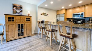A kitchen with wooden cabinets, a stainless steel refrigerator, a microwave, and a granite countertop.