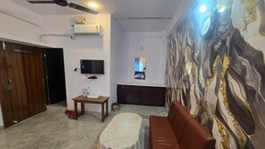 A living room with a brown sofa, a small table with a glass, a ceiling fan, and a TV mounted on the wall.