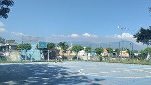 An outdoor basketball court with a fence, trees, and buildings in the background.