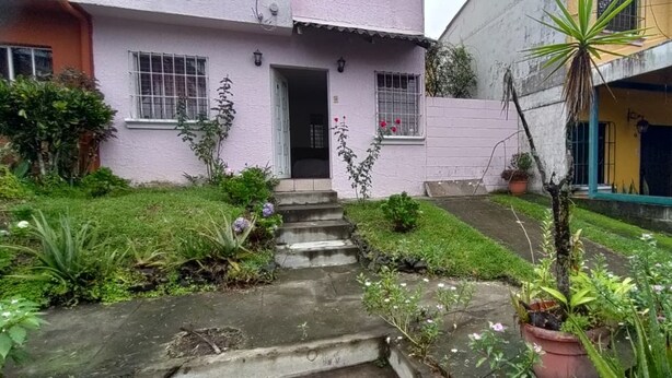 A two-story house with a front entrance, a small garden with steps leading up to the door, and a car parked in the driveway.