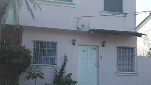 A two-story house with a white door marked "H 22", a small balcony, and a garden area with various plants.