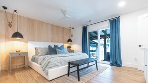 A modern bedroom with a large bed, bedside tables, a bench, and a view of the outdoors. - Little Canal, Pool, Hot Tub, Cold Plunge, Sauna (Santa Rosa Beach)