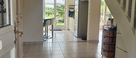 A spacious hallway with a black doormat, a dining area with a table and chairs, a refrigerator, and a staircase.