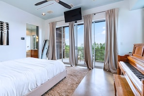 A bedroom with a bed, a piano, a TV, and a balcony with curtains.