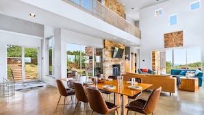 A spacious living area with a high ceiling, a stone fireplace, and a large dining table set for six.