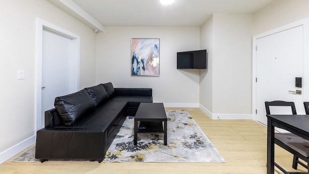 Uma sala de estar moderna com um sofá de couro preto, uma mesa de centro e uma TV fixada na parede.