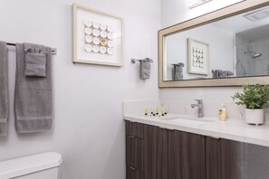 A bathroom with a white sink, a mirror, and a framed artwork on the wall. - The Penn Hotel - Immerse in Gaslamp Vibes from this Stylish 2BR! (San Diego)