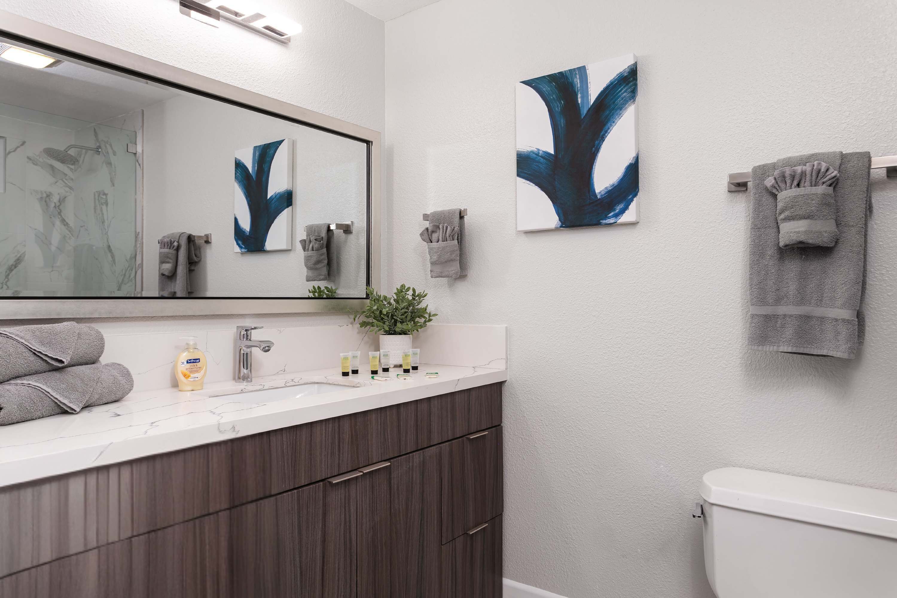 A bathroom with a white sink, dark wooden cabinets, a white toilet, and two abstract paintings on the wall.