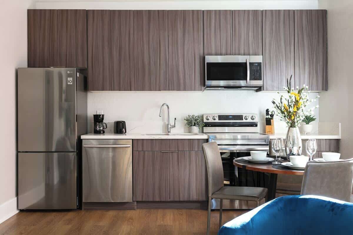 A modern kitchen with dark wood cabinets, stainless steel appliances, and a dining area with a blue chair.