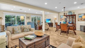 A spacious living area with a sofa, dining table, and chairs, a television, and a large window with a view of greenery. - Gulf Gate Dream 2bd 2ba Htd Pool Beaches Shopping (Sarasota)