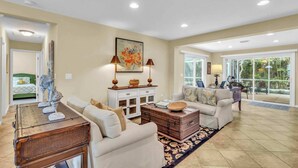 A spacious living room with a large window, a white sofa, a coffee table, and a dining area with a white cabinet and a painting on the wall. - Gulf Gate Dream 2bd 2ba Htd Pool Beaches Shopping (Sarasota)
