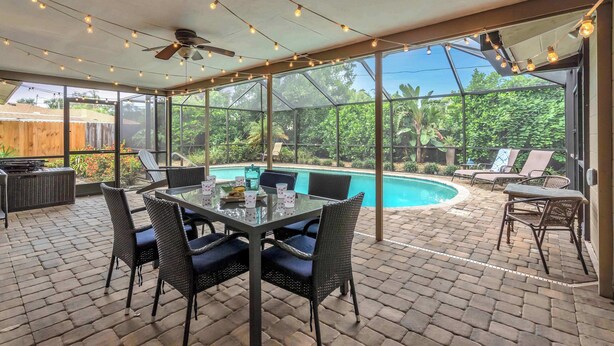 Une terrasse extérieure avec une table et des chaises en verre, une piscine et une vue sur la verdure.