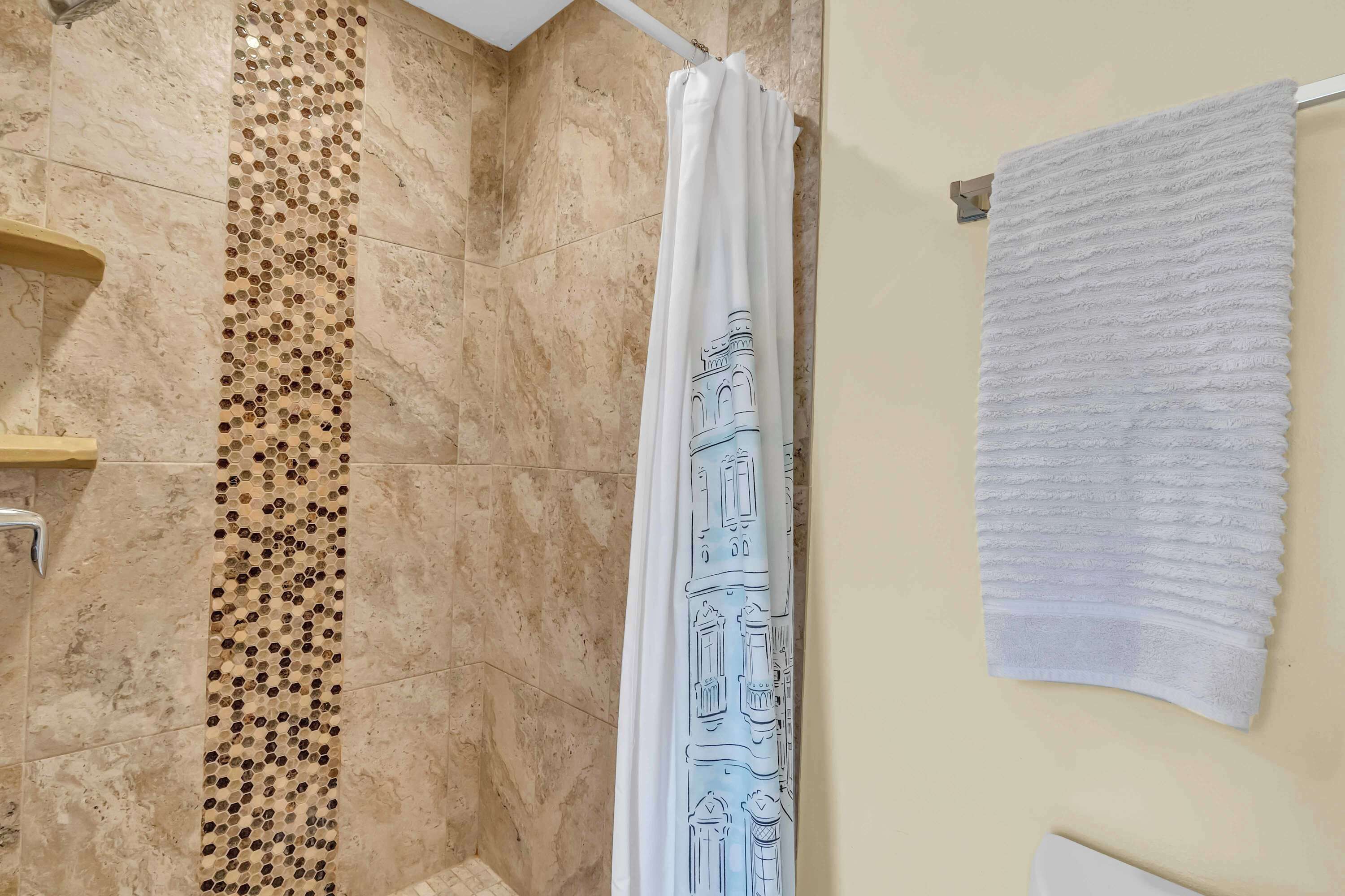 Een badkamer met een douchegordijn met een gebouwillustratie, een witte handdoek aan de muur en een decoratieve tegelrand.