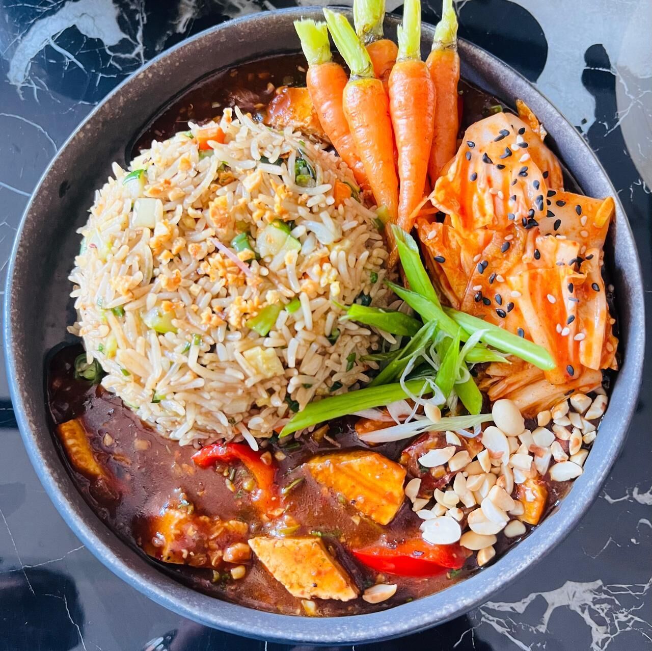 Un bol contenant des aliments, du riz, des carottes et une sauce foncée.