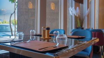 A restaurant setting with a table set for two, featuring a clear glass top, a brown menu, and cutlery.