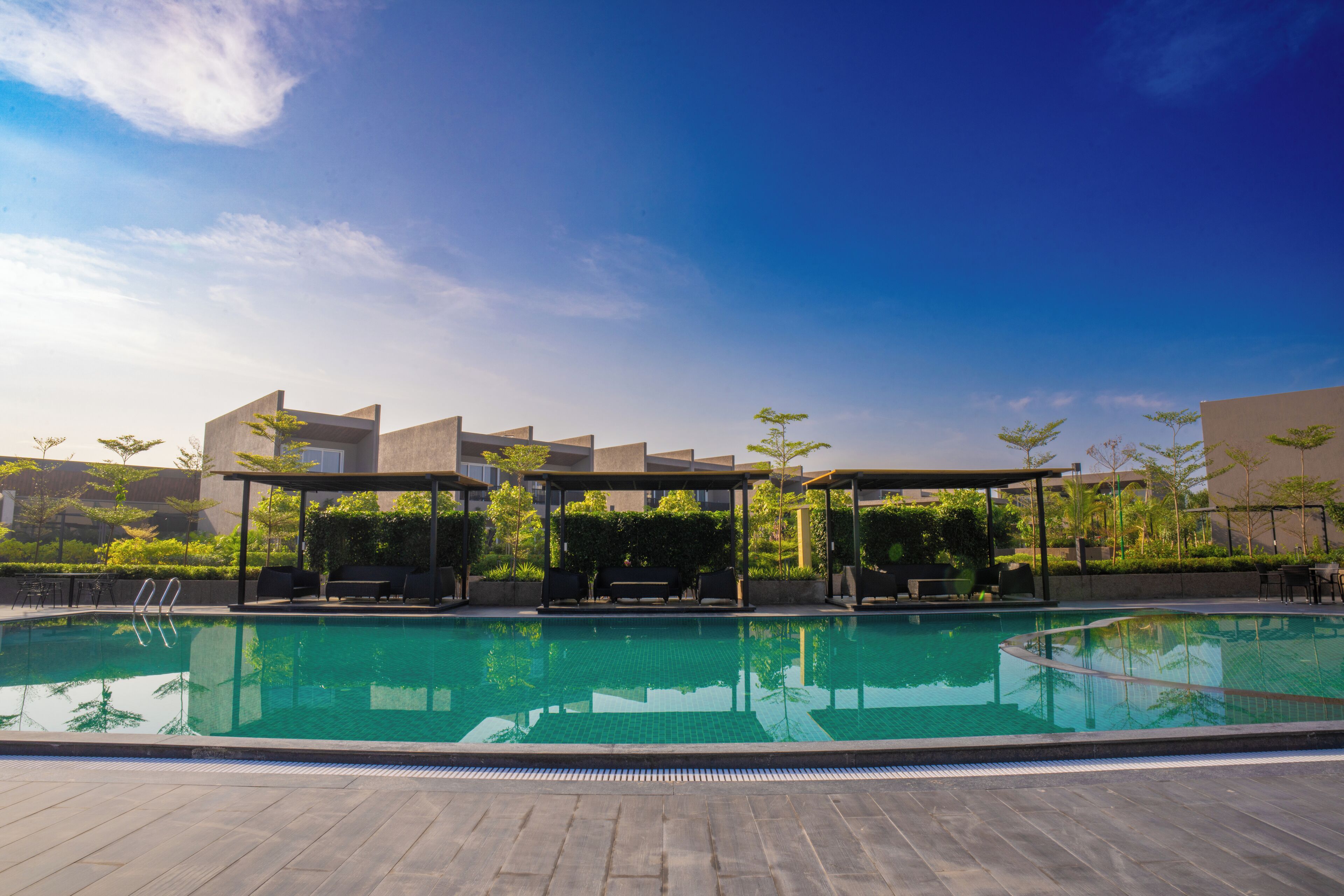 A modern outdoor pool area with a clear blue sky, surrounded by buildings and greenery.