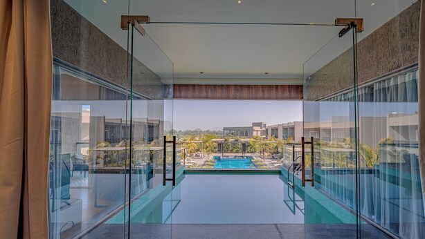 A modern hotel room with a glass wall, a pool, and a view of the surrounding buildings. - AMARTARA THE RESORT (Abu Road)
