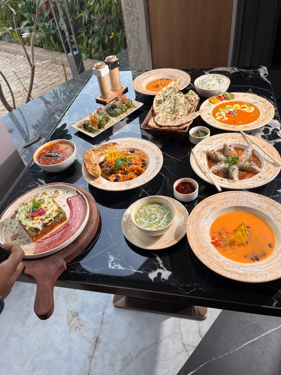 A table with various dishes, including a slice of pizza, a bowl of soup, and several plates of food.