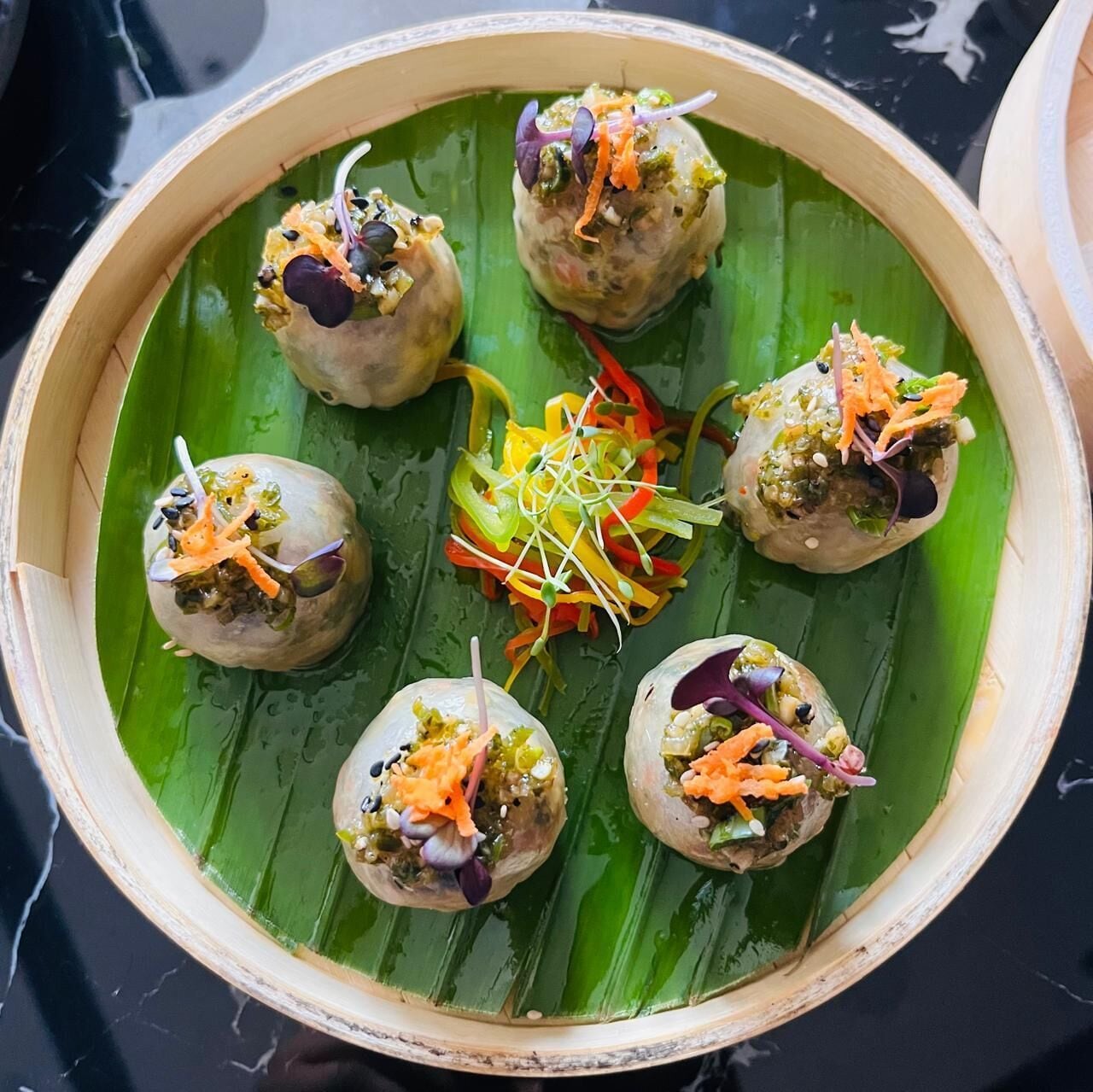 A bamboo steamer with food items on a green leaf.