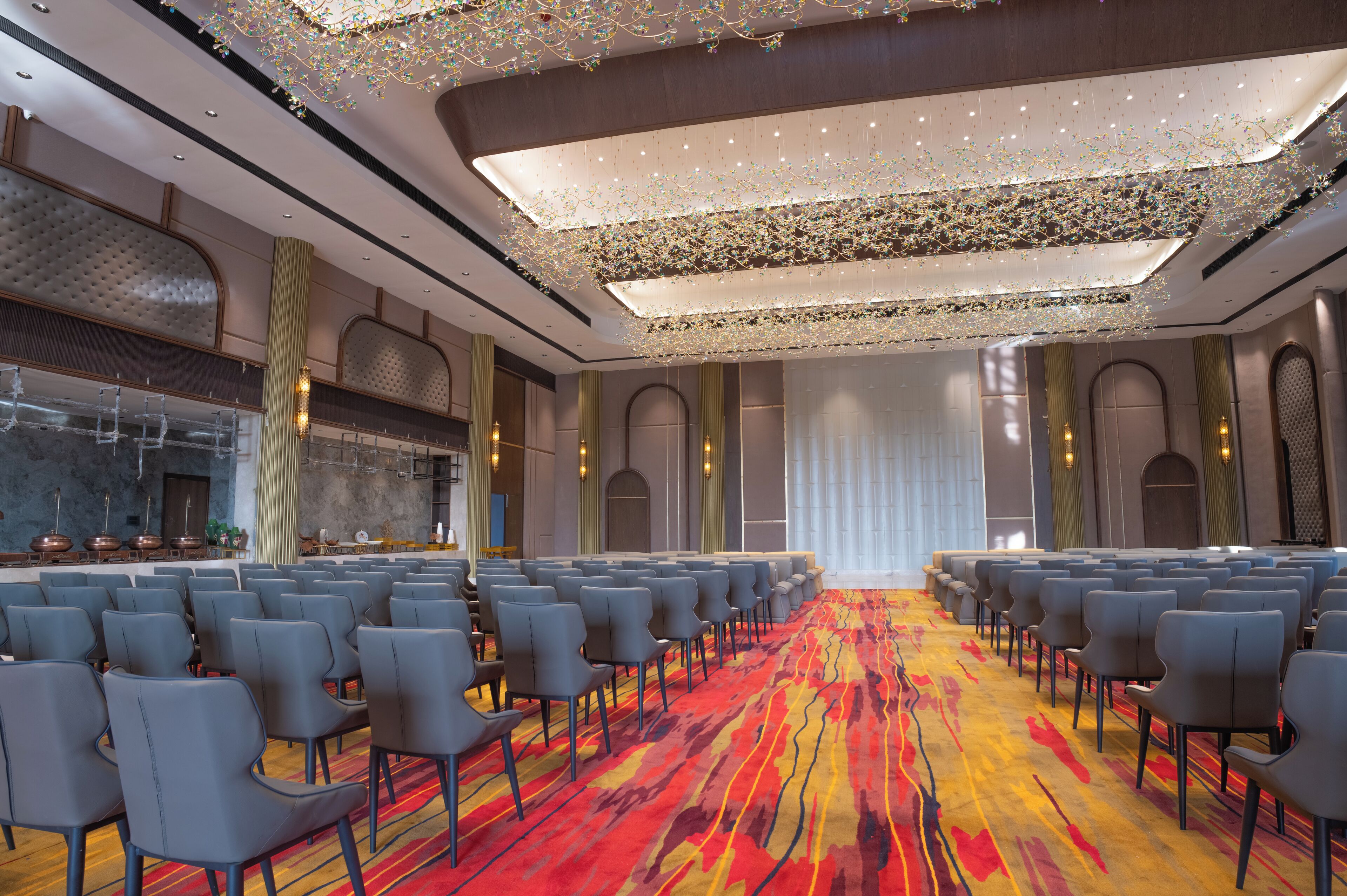 A conference room with rows of chairs, a colorful carpet, and a modern chandelier.