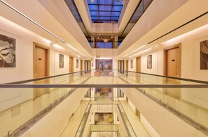 A hotel corridor with a glass floor, wooden doors, and artwork on the walls. - Qotel Signature - Golf Course Road (Gurugram)