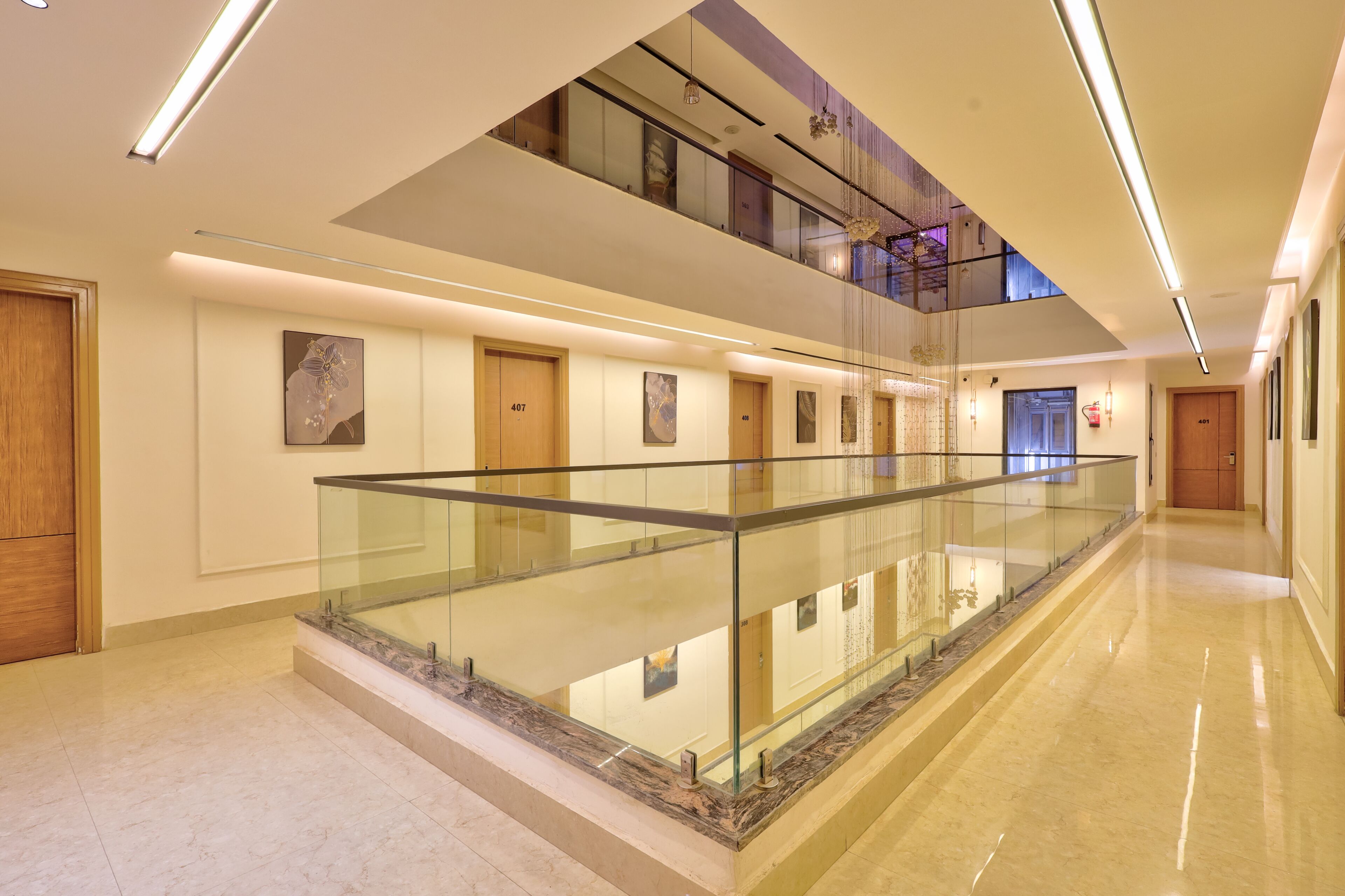 A modern hotel lobby with a glass railing, marble flooring, and a mezzanine level.