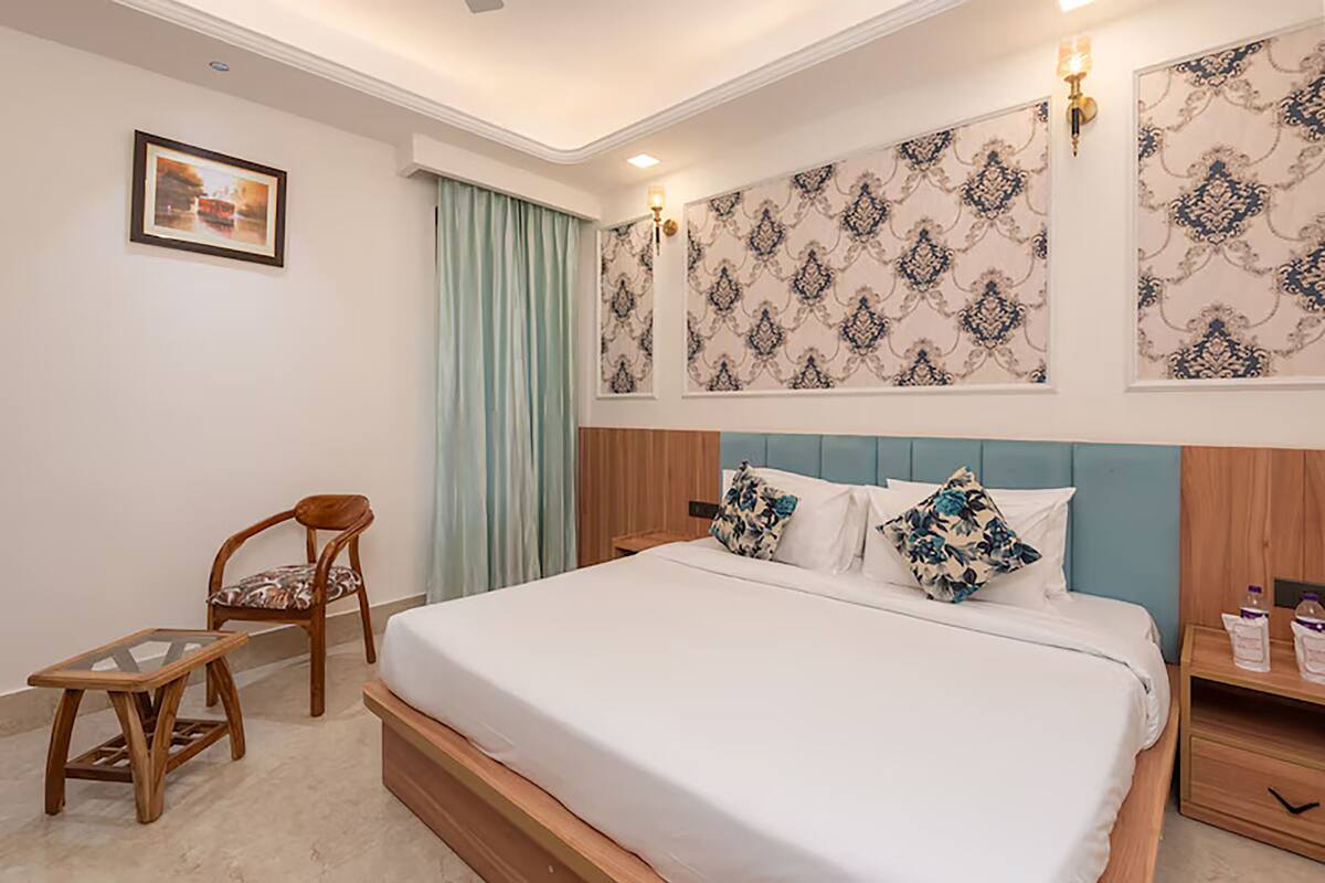 Habitación de hotel ordenada con cama, una silla, una mesita y una mesita de noche con lámpara.