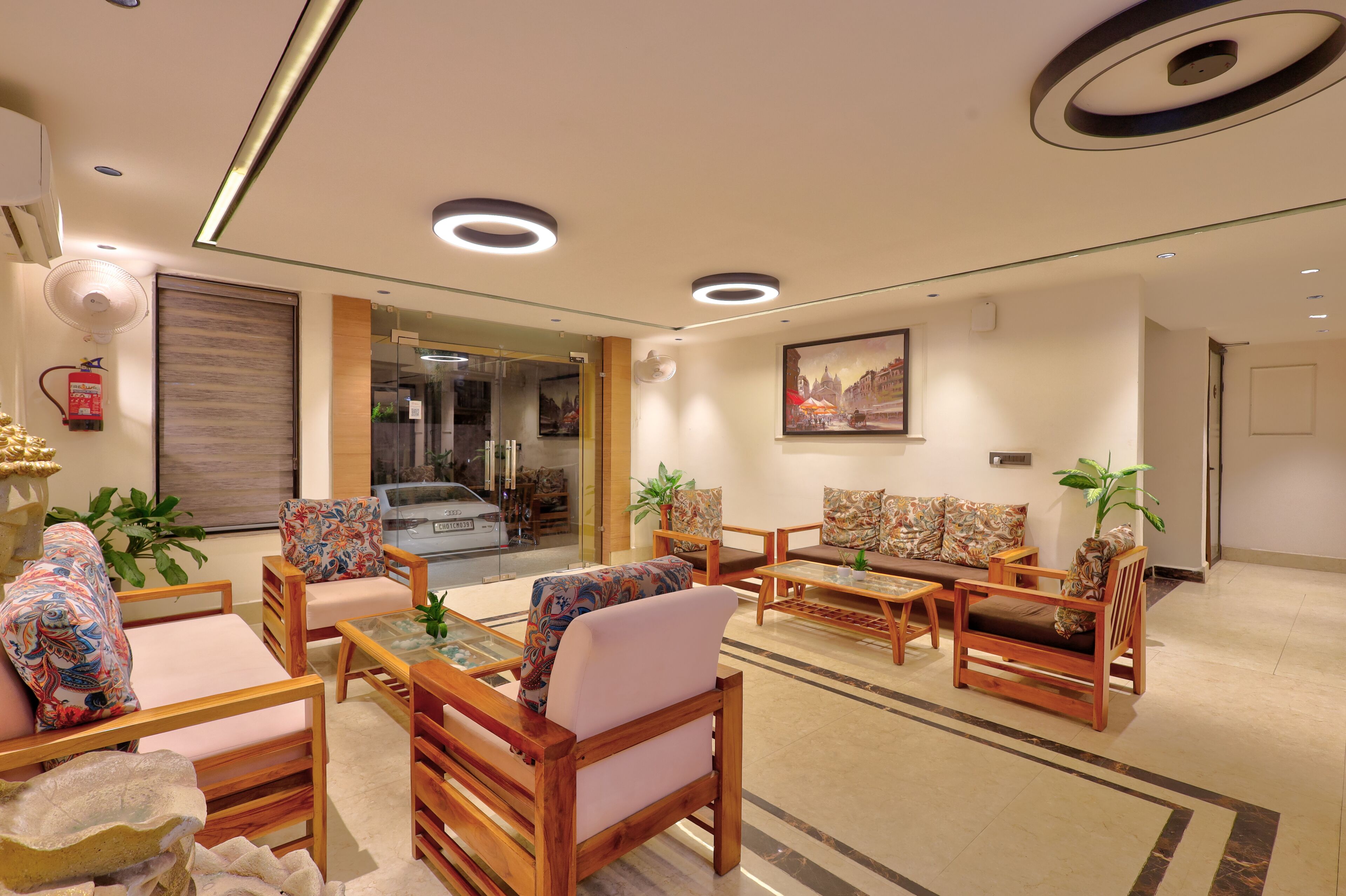 A modern hotel lobby with wooden furniture, a glass coffee table, and a fire extinguisher on the wall.