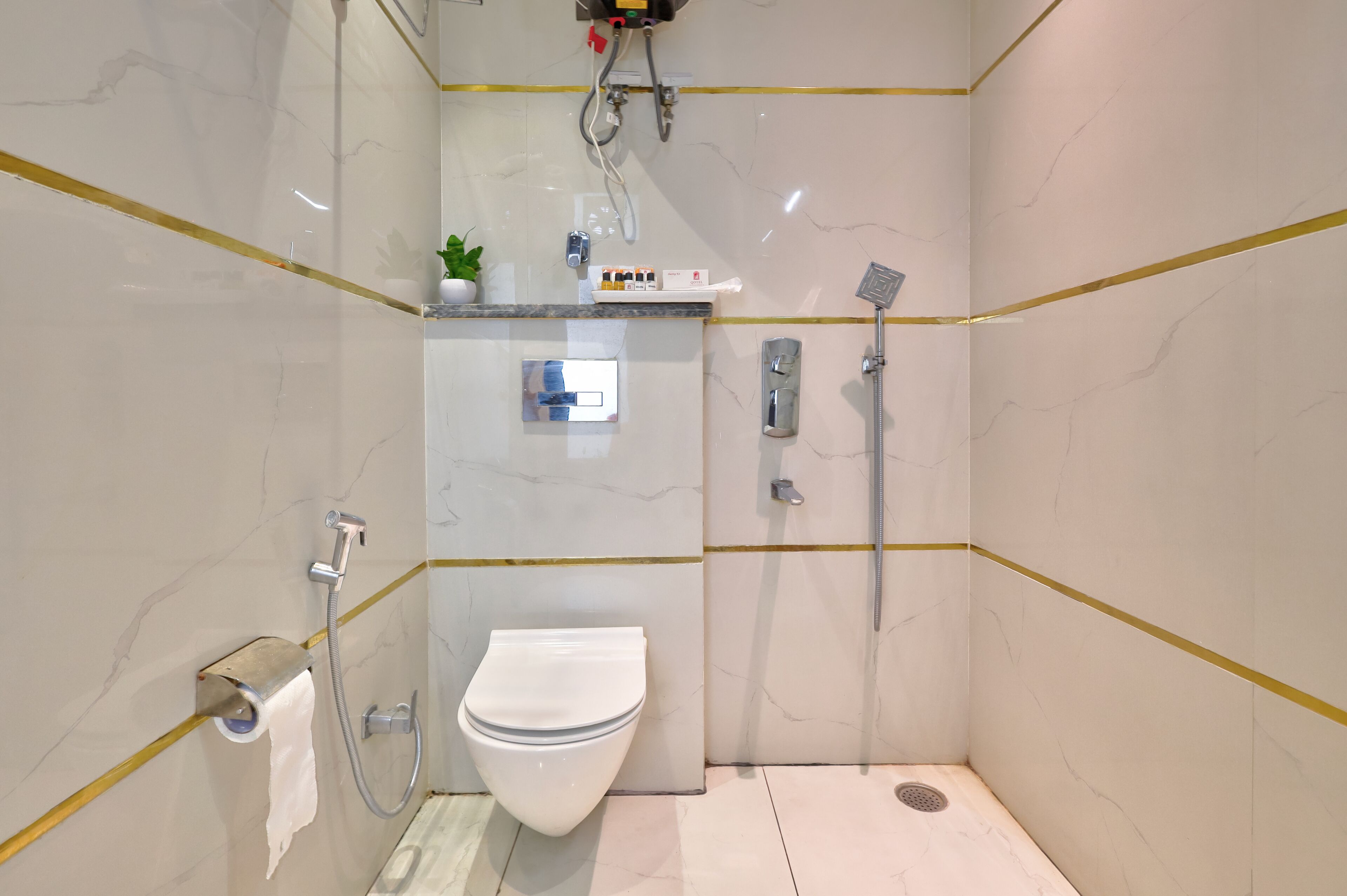 A compact, modern bathroom with a toilet, a shower, and a small shelf with toiletries.