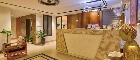 A hotel reception area with a modern design, including a reception desk, seating area, and a Buddha statue.