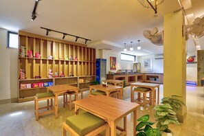 A restaurant interior with wooden tables and chairs, a counter with a menu, and shelves stocked with snacks. - Qotel Signature - Golf Course Road (Gurugram)