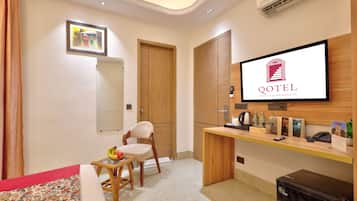 A hotel room with a bed, a desk, a chair, a television, and a minibar.