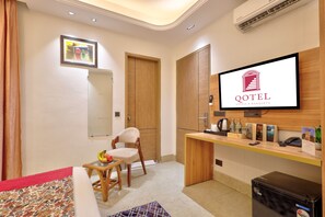 A hotel room with a bed, a desk, a chair, a television, and a minibar. - Qotel Signature - Golf Course Road (Gurugram)