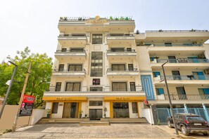 A multi-story hotel with a terrace cafe, a sign for a restaurant, and a car parked in front. - Qotel Signature - Golf Course Road (Gurugram)