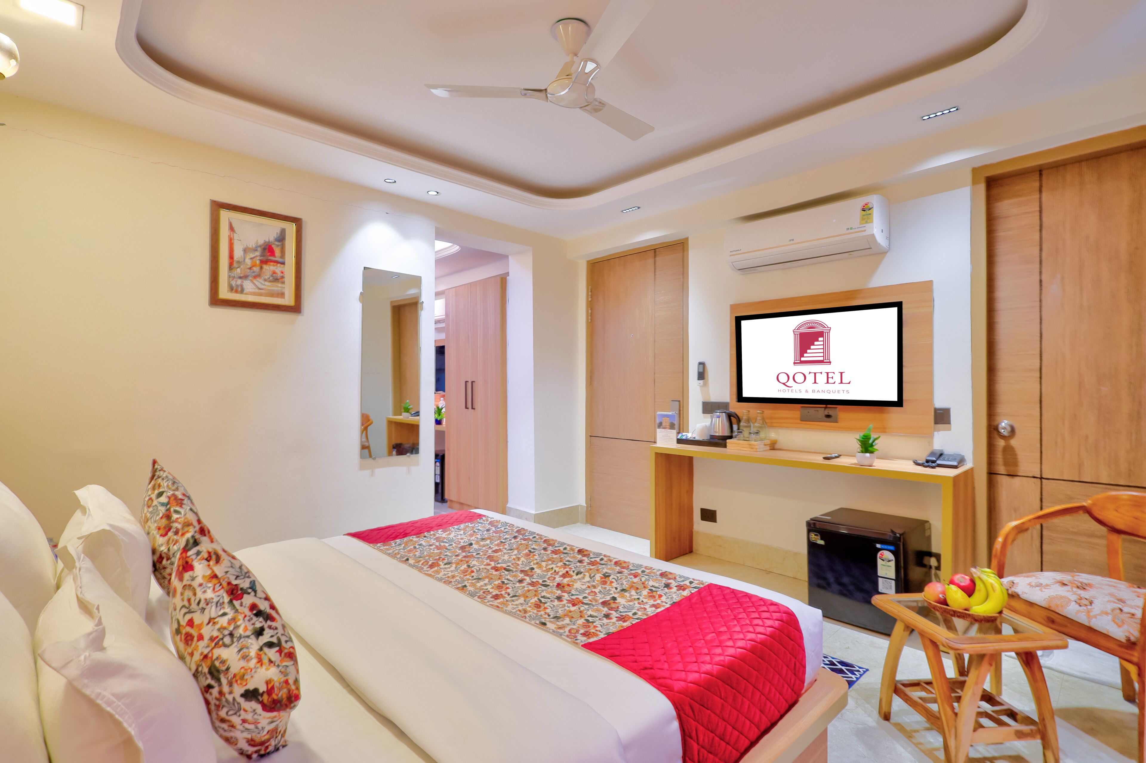 Ein Hotelzimmer mit einem Bett, einem Schreibtisch mit Computer, einem Fernseher und einem kleinen Tisch mit Obst.