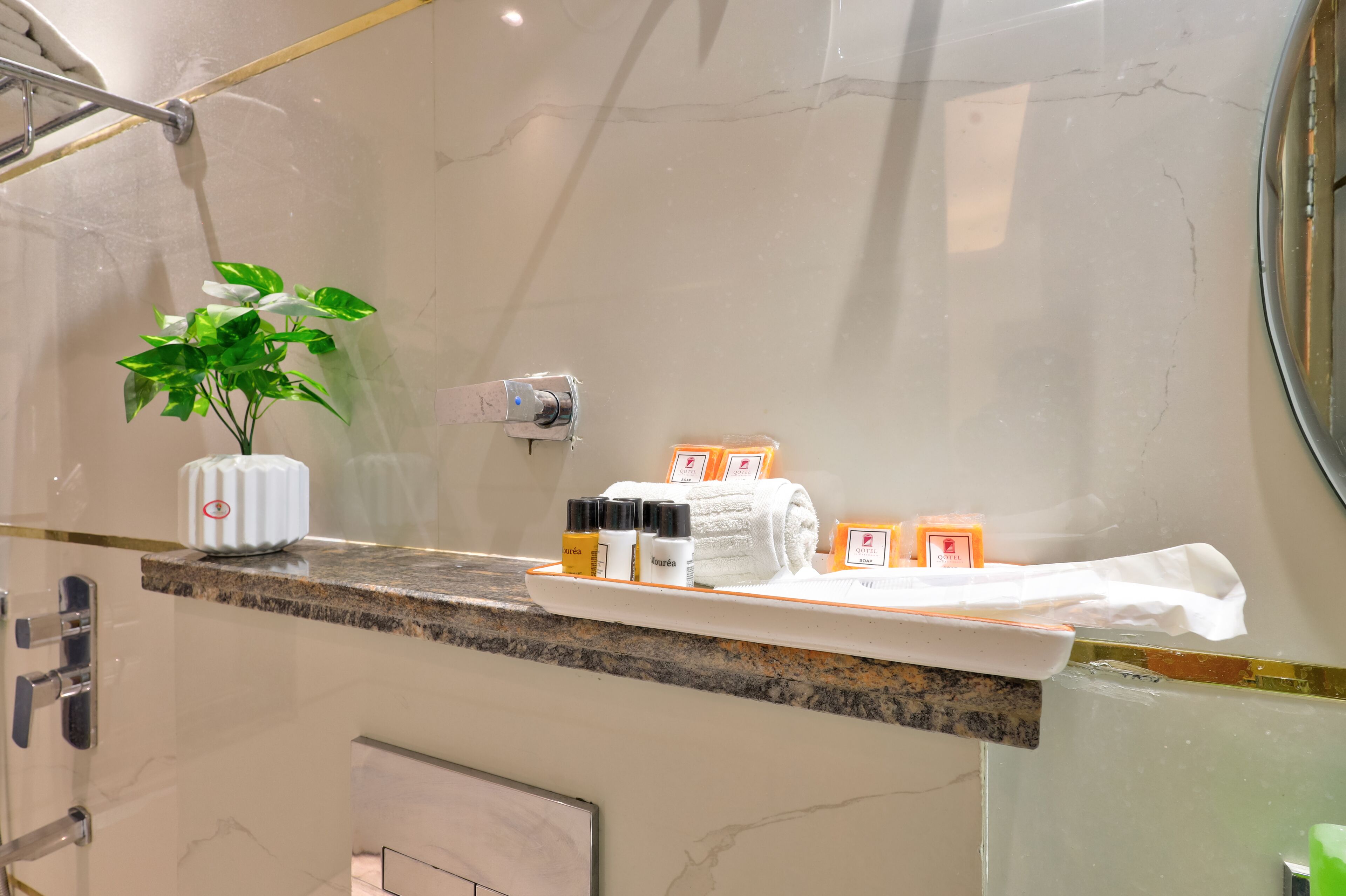 Un baño con encimera de mármol, una planta, artículos de aseo y un perchero para toallas.