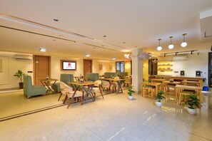 Eine Hotelhalle mit Sitzbereichen, einem Empfangstresen und einem Fernseher, der den Namen des Hotels zeigt.