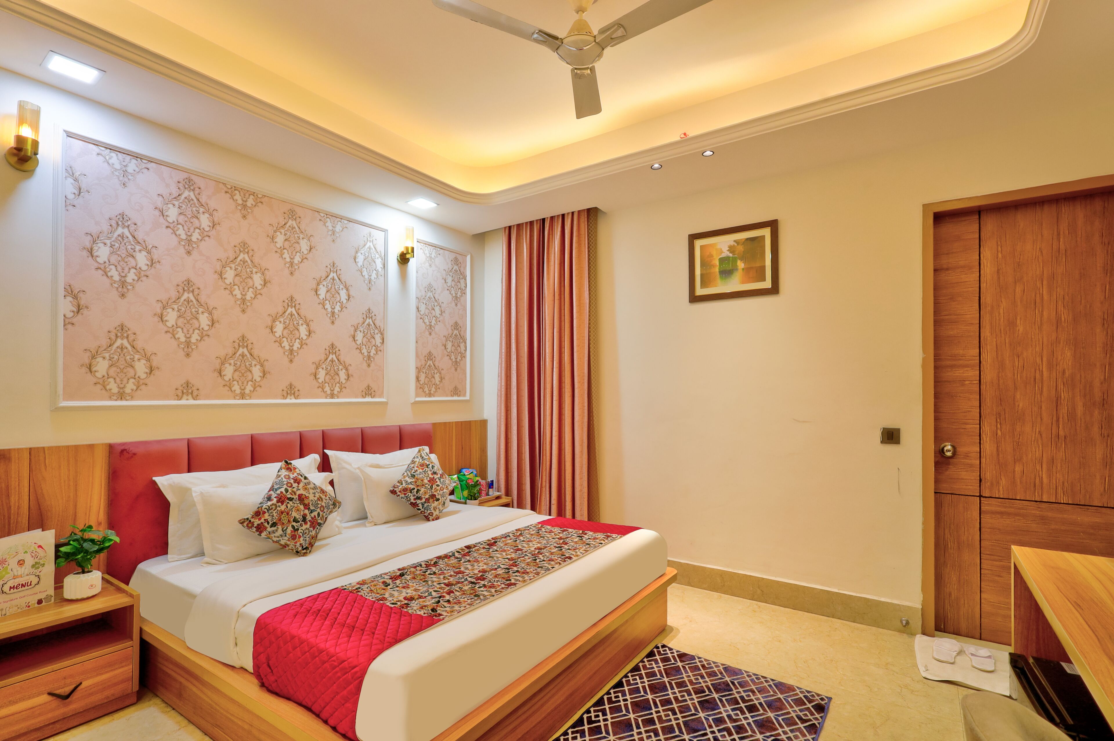 A hotel room with a bed, a nightstand, a wooden wardrobe, a ceiling fan, and a wall-mounted picture.