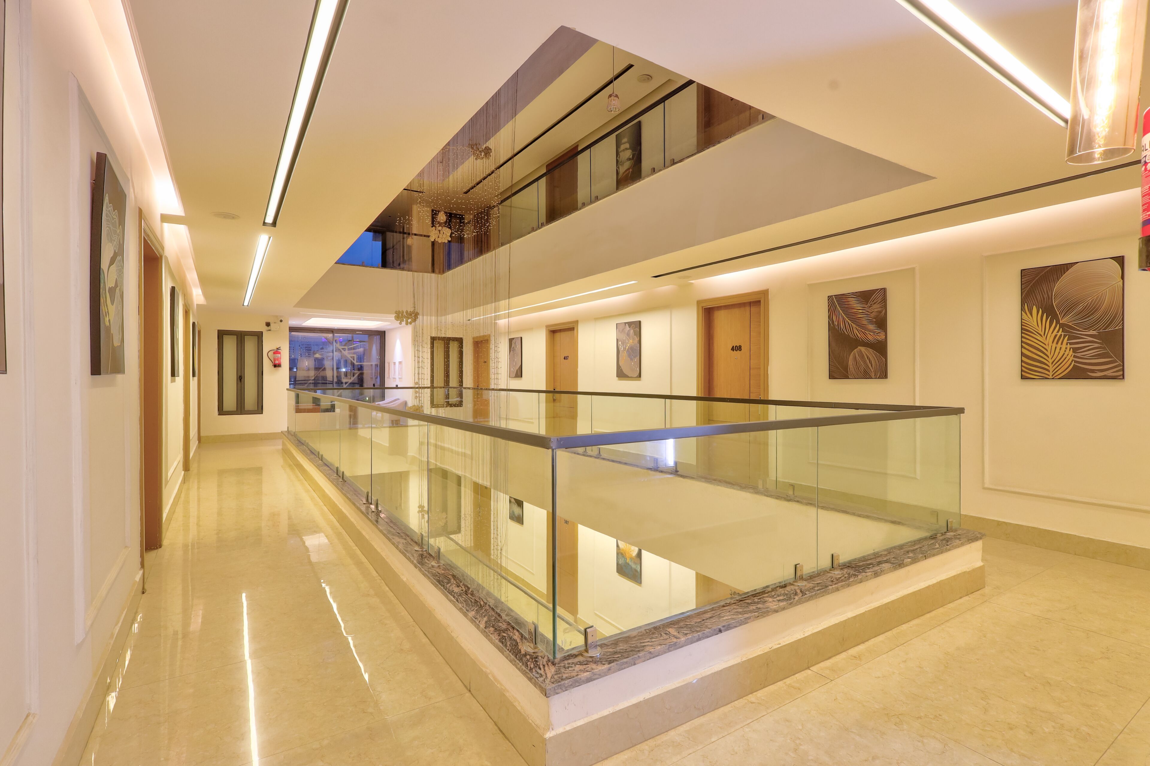 A modern hotel corridor with a glass railing, polished floors, and artwork on the walls.