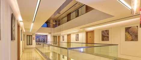 A modern hotel corridor with a glass railing, polished floors, and artwork on the walls.