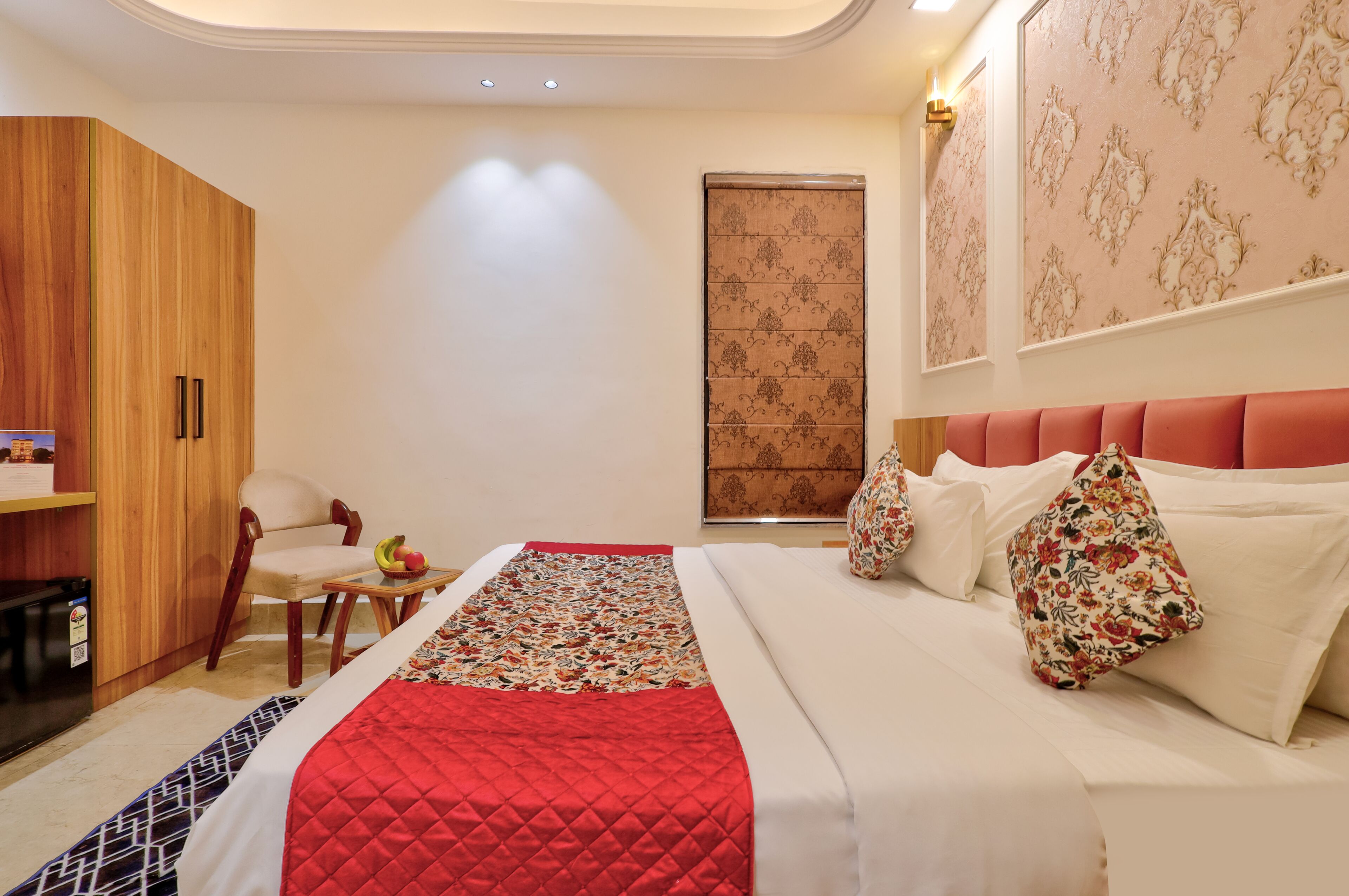 A hotel room with a bed, a chair, a small table with fruit, and a wardrobe.