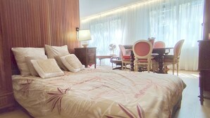 A hotel room with a large bed, a desk with a chair, and a window with curtains.